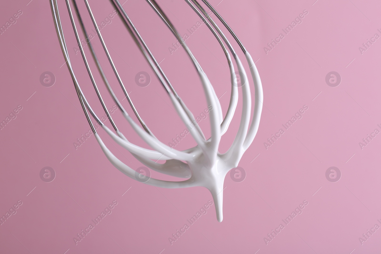 Photo of Whisk with whipped cream on pink background, closeup