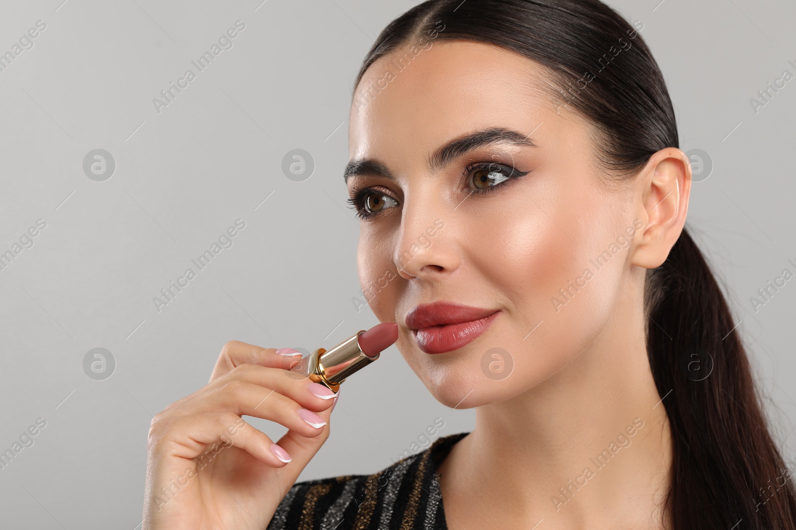Photo of Everyday makeup. Beautiful woman applying lipstick on light grey background, space for text