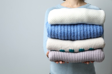 Woman holding pile of winter sweaters on grey background, closeup view. Space for text