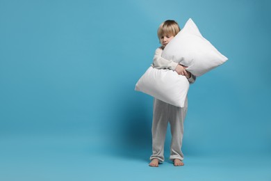 Boy in pajamas hugging pillow on light blue background, space for text