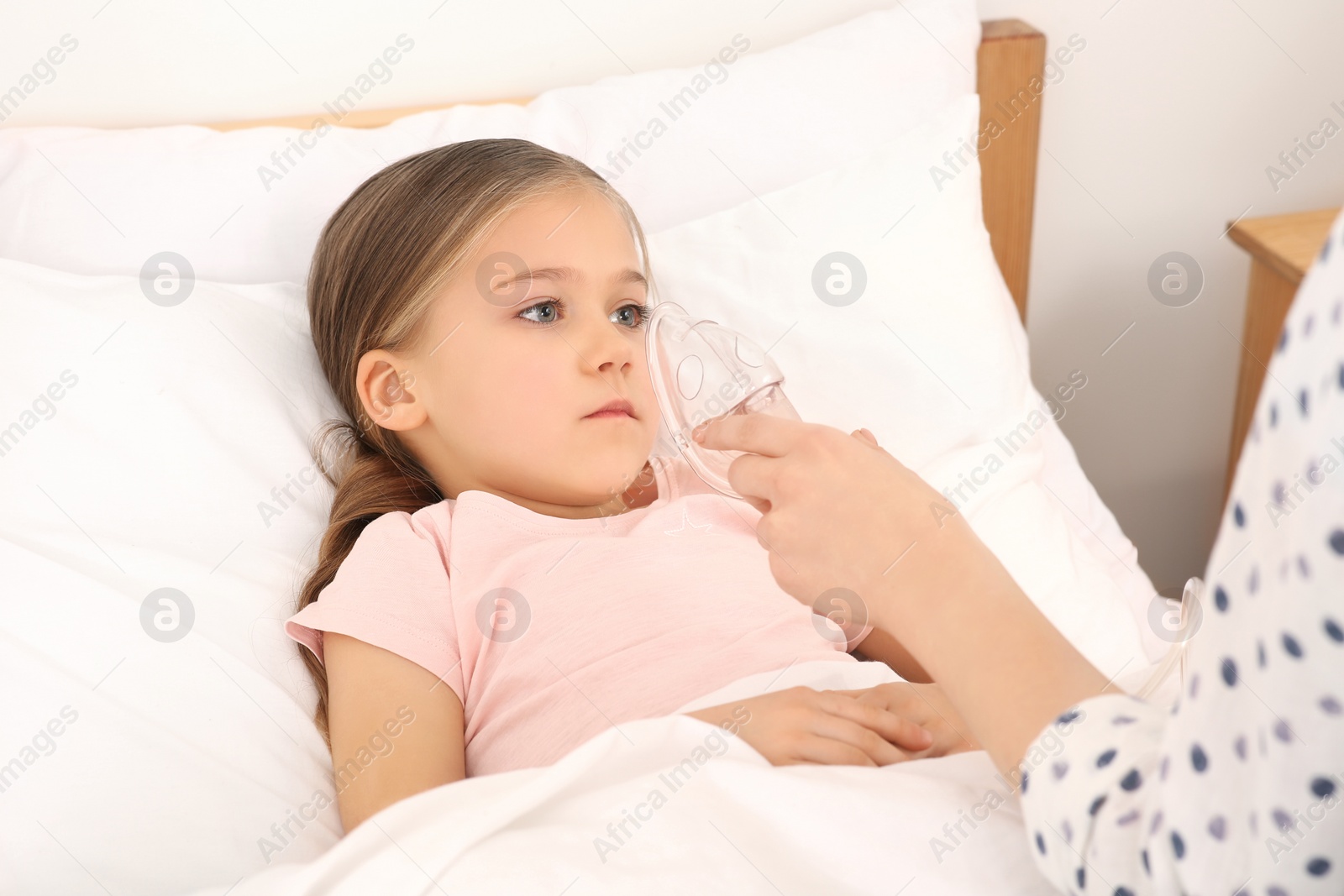 Photo of Mother helping her sick daughter with nebulizer inhalation in bedroom, closeup