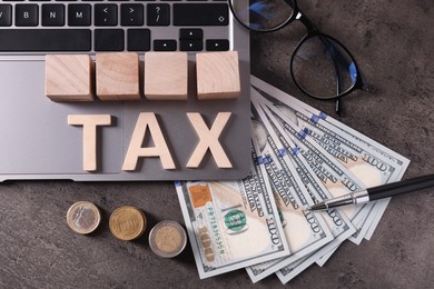 Word Tax made of wooden letters, cubes, laptop, banknotes and coins on grey table, flat lay