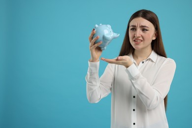 Sad woman with piggy bank on light blue background, space for text