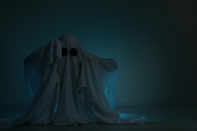 Photo of Creepy ghost. Woman covered with sheet on dark background, space for text