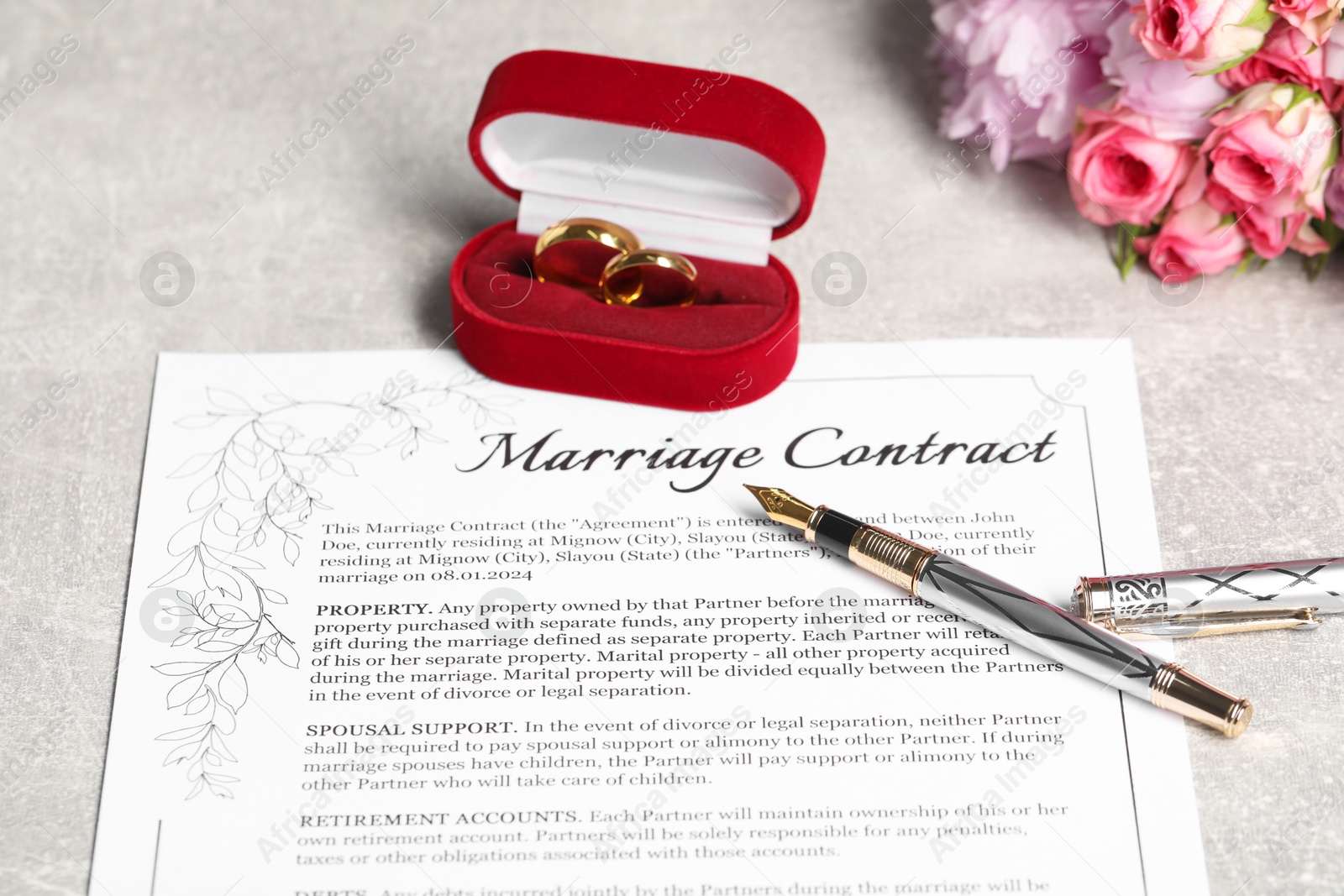 Photo of Marriage contract, fountain pen, golden wedding rings and flowers on grey table