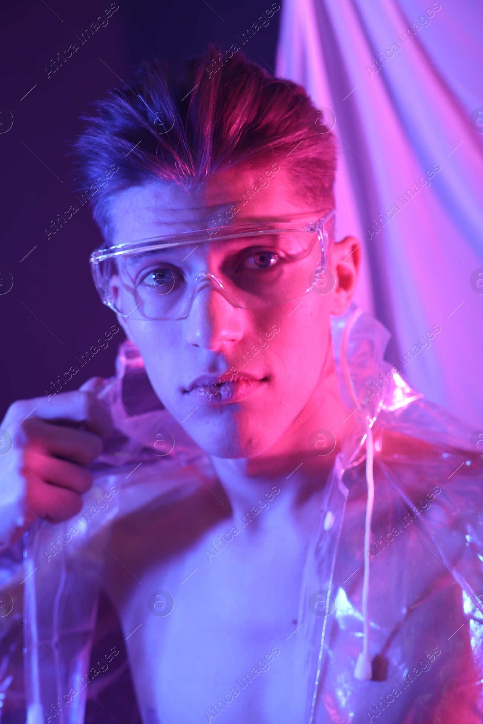 Photo of Stylish young man wearing clear coat and glasses in neon lights