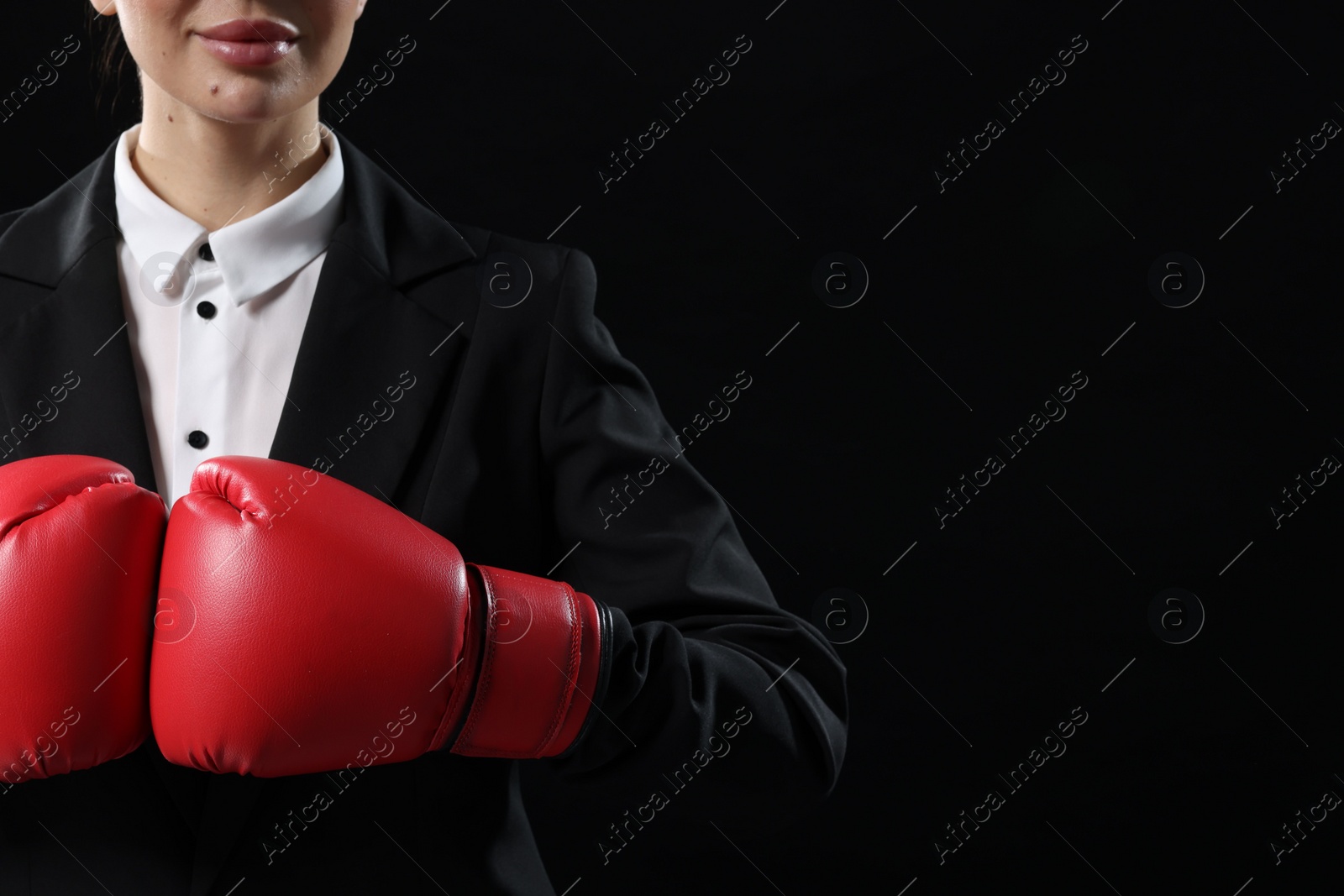 Photo of Businesswoman in suit wearing boxing gloves on black background, closeup. Space for text