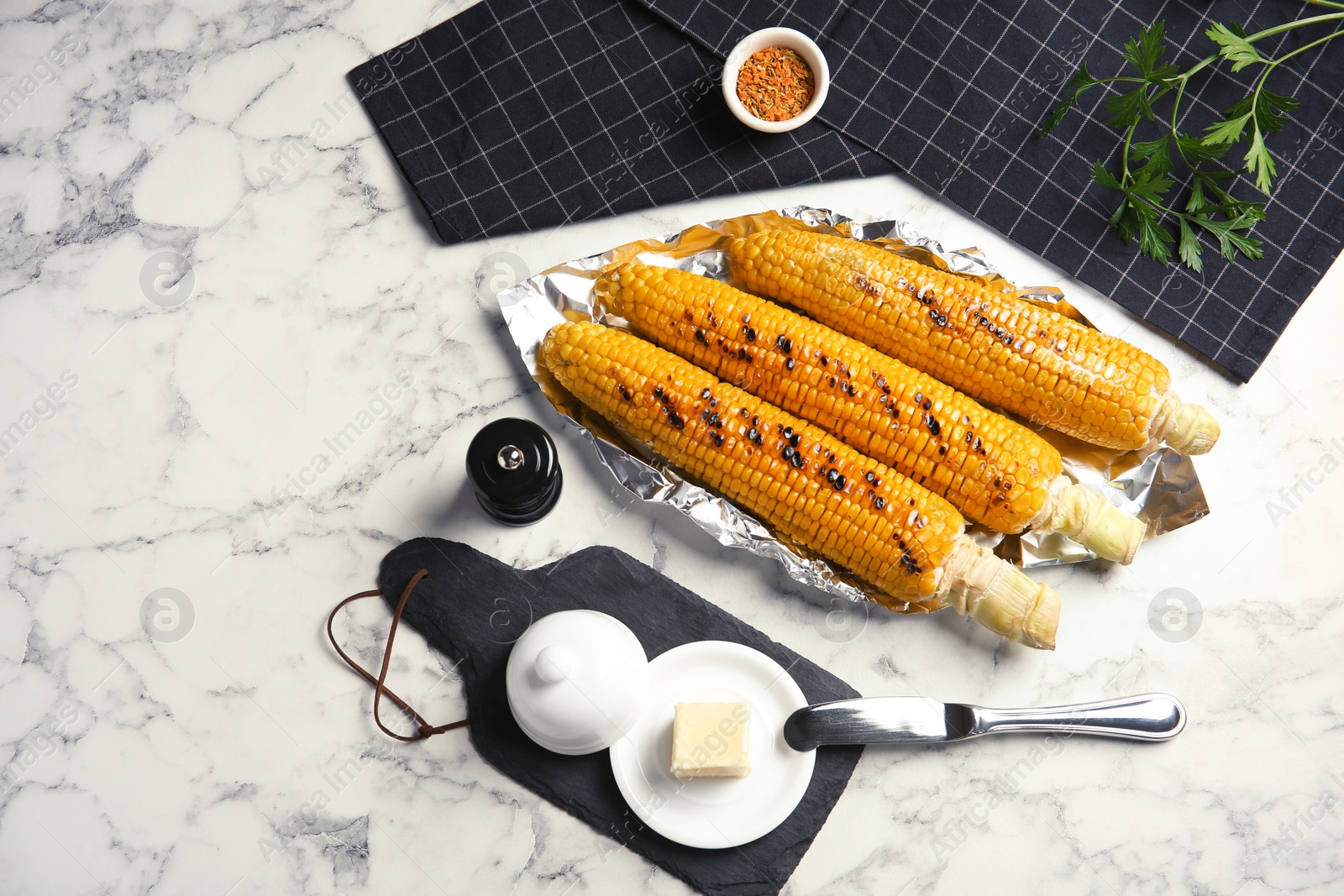 Photo of Fresh grilled tasty corn cobs served with butter on marble table, top view