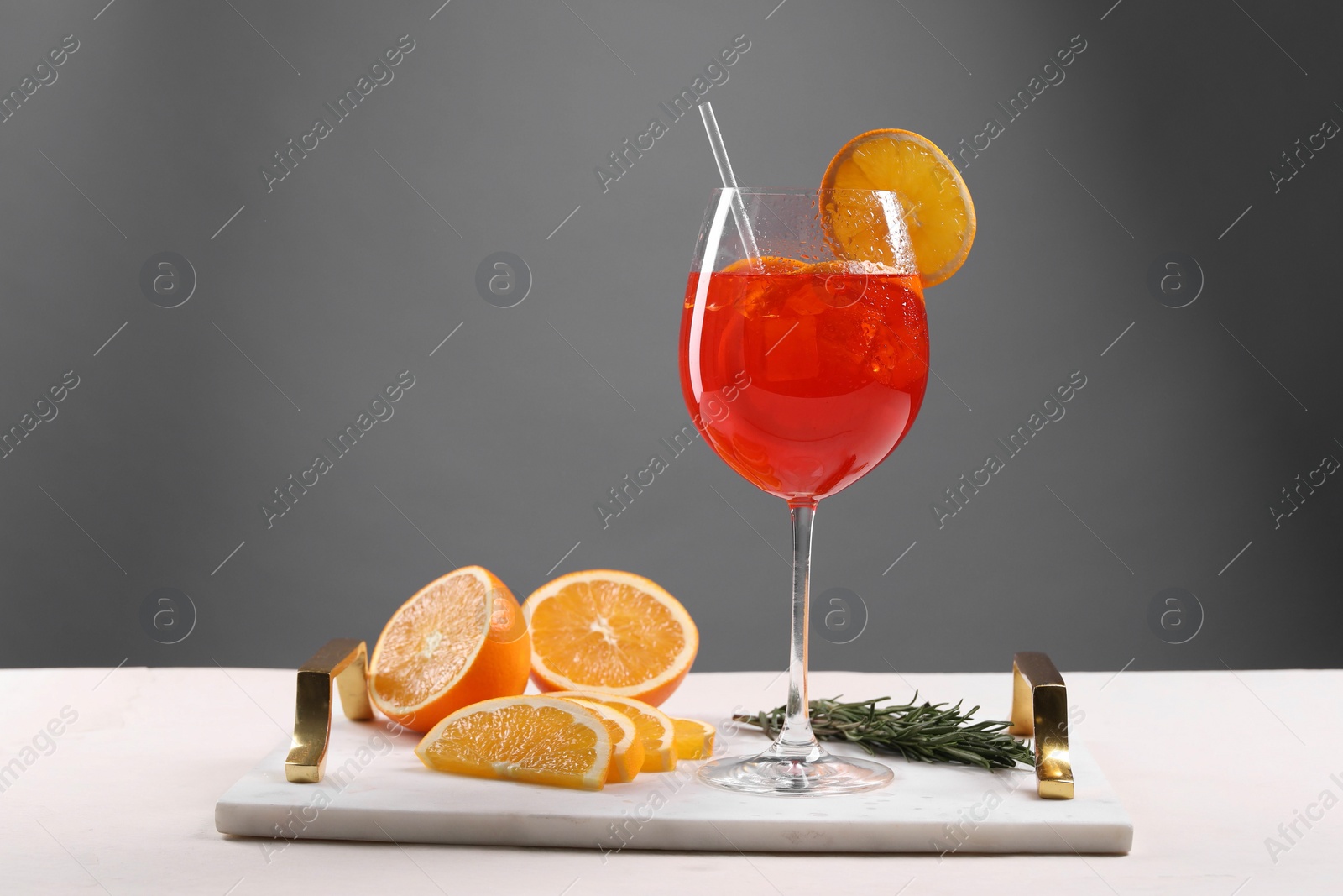 Photo of Glass of tasty Aperol spritz cocktail with orange slices and rosemary on white table against gray background, space for text