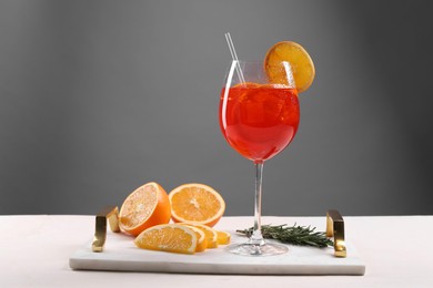 Glass of tasty Aperol spritz cocktail with orange slices and rosemary on white table against gray background, space for text