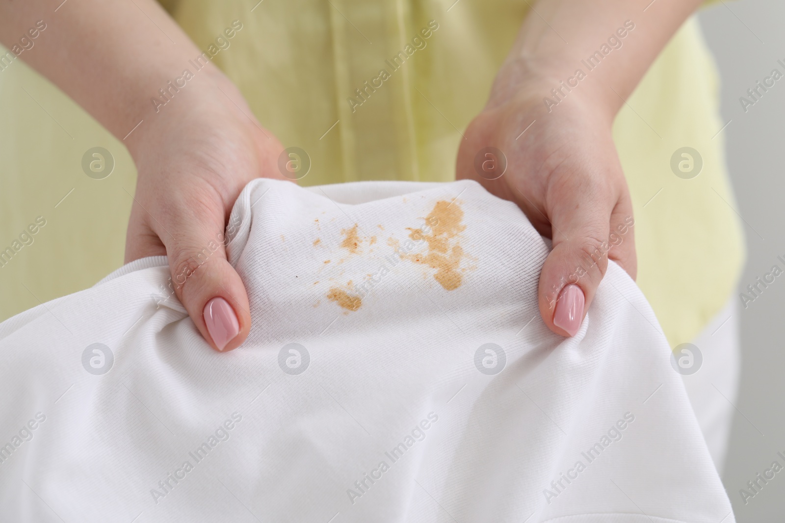 Photo of Woman holding shirt with stain against light grey background, closeup