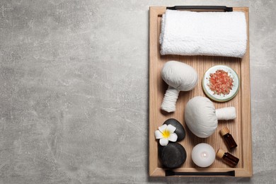 Herbal massage bags, spa stones, sea salt, essential oils and towel on grey table, top view. Space for text