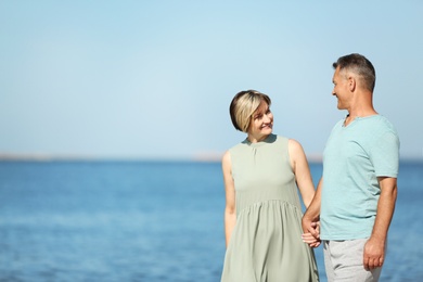 Happy mature couple holding hands at beach on sunny day