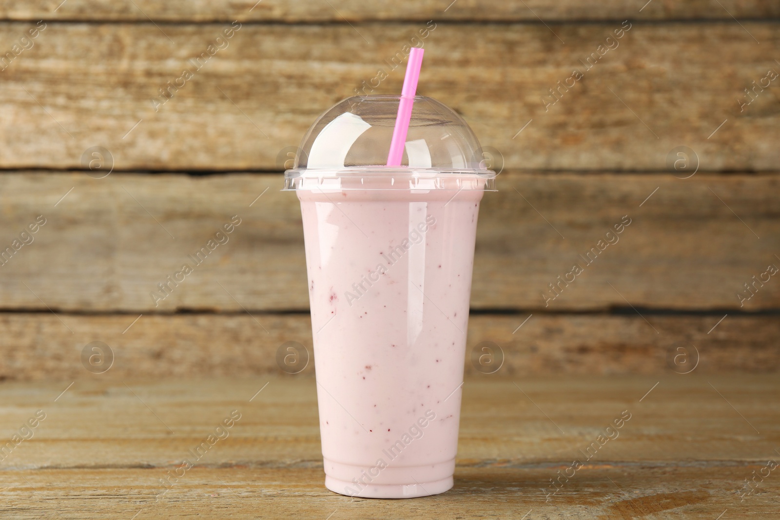 Photo of Plastic cup of tasty smoothie on wooden table