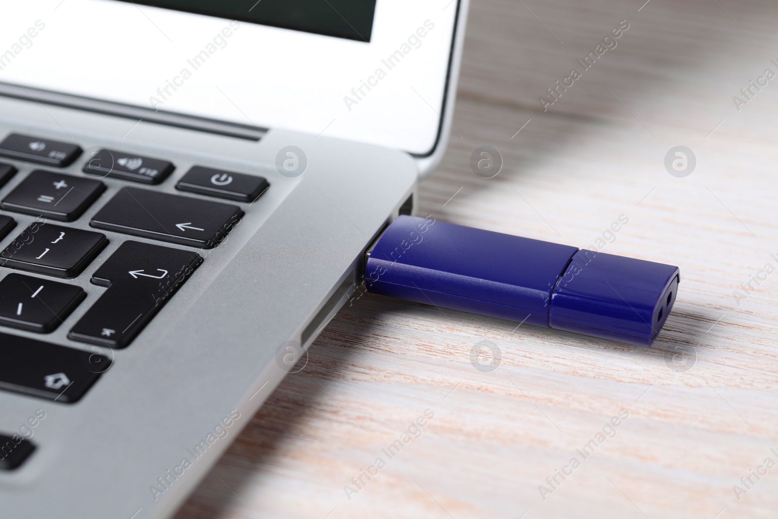 Photo of Usb flash drive attached into laptop on white wooden table, closeup