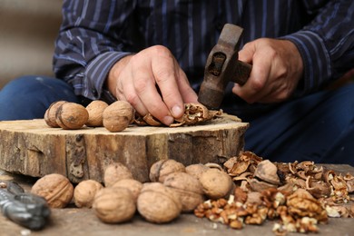 Photo of Man cracking walnuts with hammer at wooden table, closeup