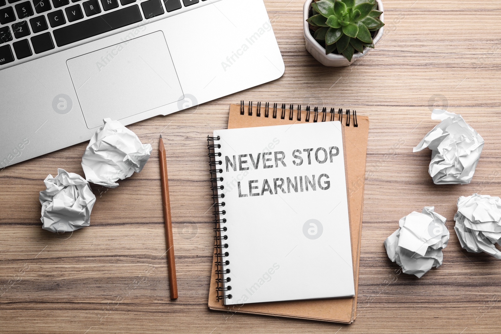 Image of Notebook with phrase NEVER STOP LEARNING and crumpled paper on wooden table, flat lay