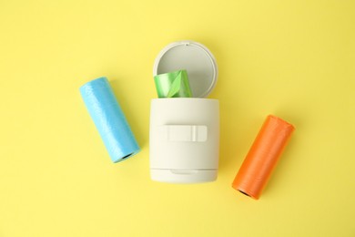 Dog waste bags and dispenser on yellow background, flat lay