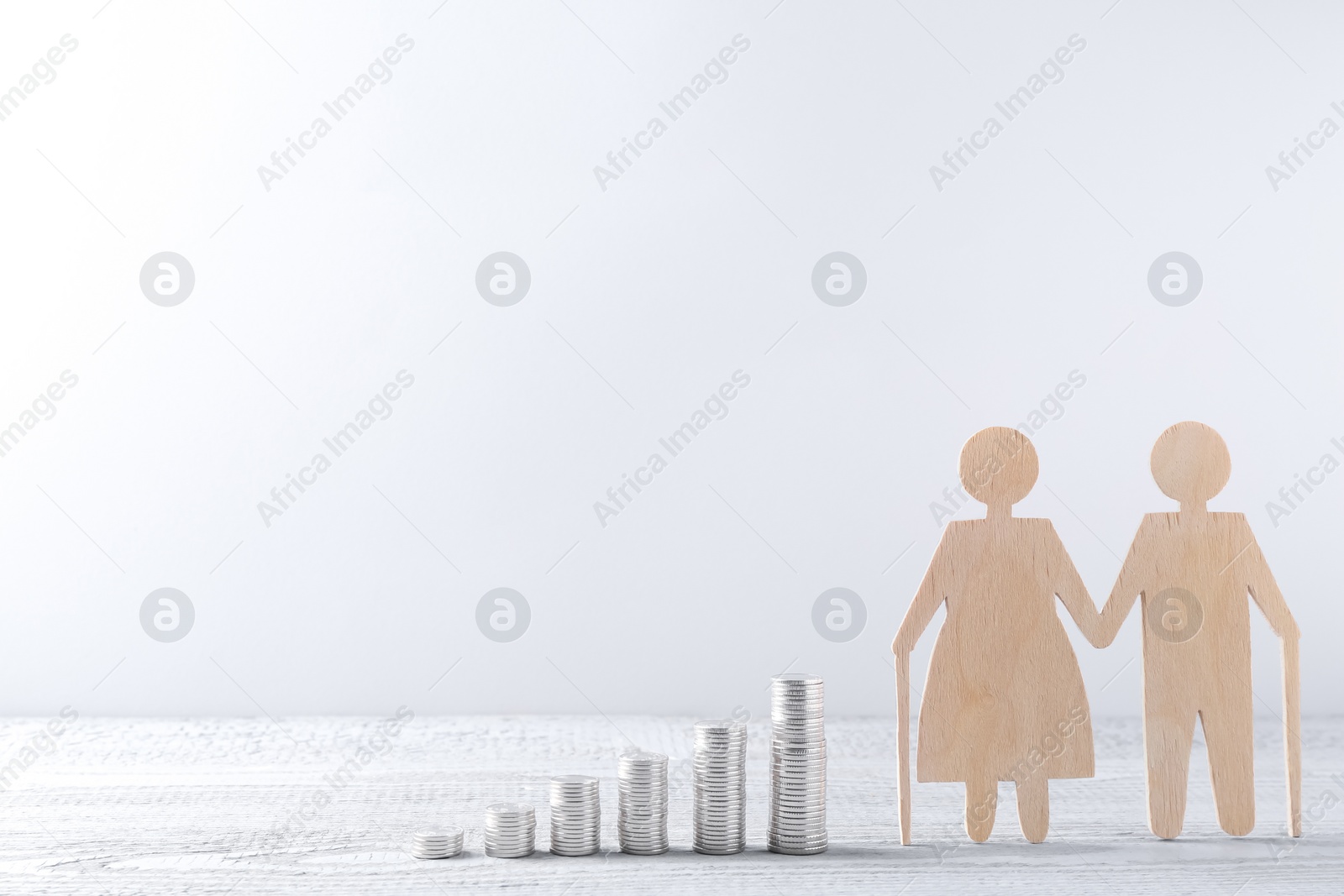 Photo of Pension savings. Figure of senior couple and stacked coins on grey wooden table, space for text