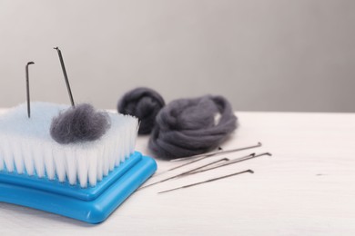 Photo of Felting tools and wool on light wooden table, closeup. Space for text
