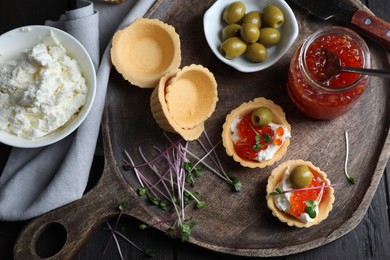 Photo of Delicious tartlets with red caviar and cream cheese served on wooden table, flat lay