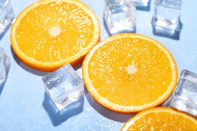 Slices of juicy orange and ice cubes on light blue background, closeup