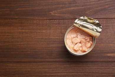Photo of Can of conserved tuna on wooden table, top view. Space for text