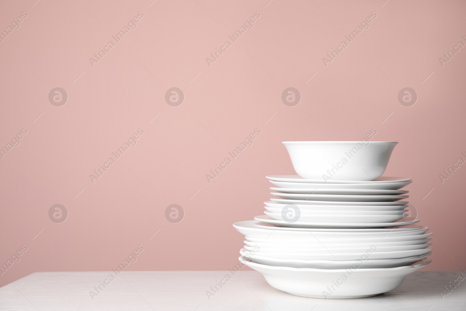 Photo of Stack of clean plates on white table against pink background. Space for text