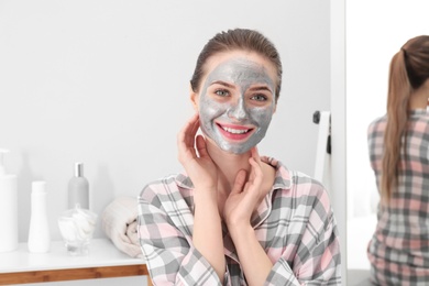 Photo of Young woman with cleansing mask on her face in bathroom. Skin care