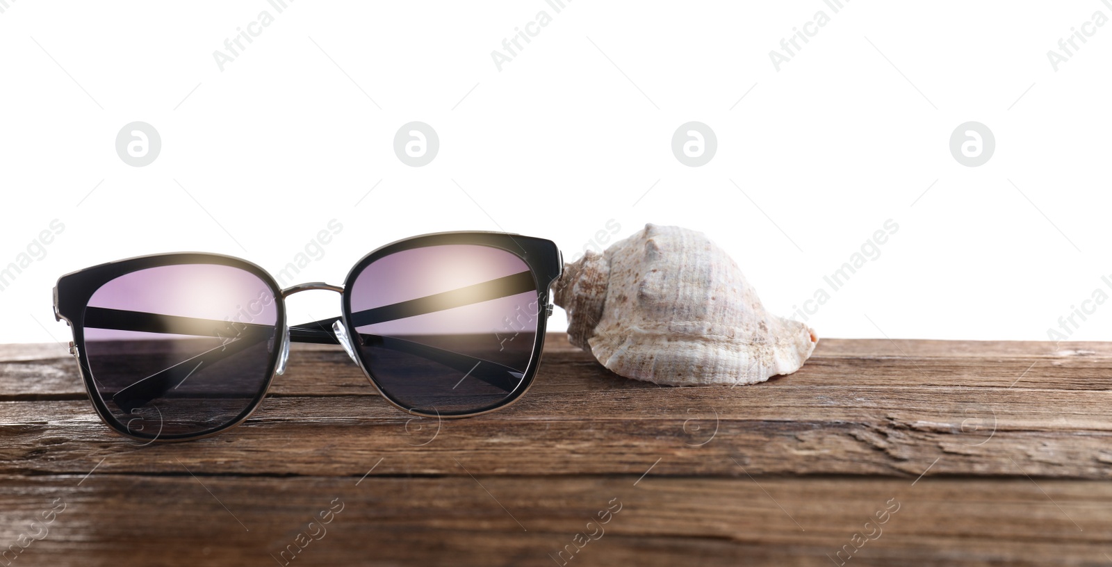 Photo of Stylish sunglasses and shell on wooden table against white background