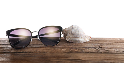 Stylish sunglasses and shell on wooden table against white background