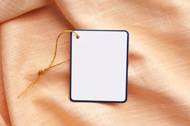Photo of Cardboard tag with space for text on pale orange fabric, top view