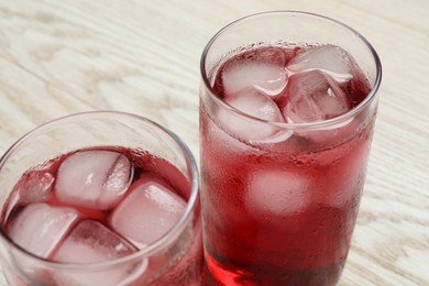 Photo of Glasses of delicious iced hibiscus tea on white wooden table, closeup
