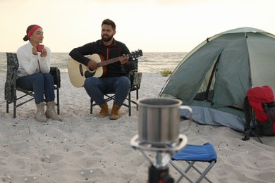 Lovely couple resting near camping tent on sandy beach