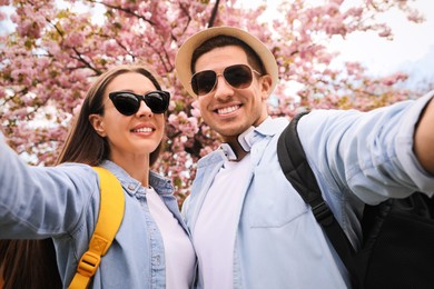 Happy couple taking selfie near blossoming sakura outdoors on spring day