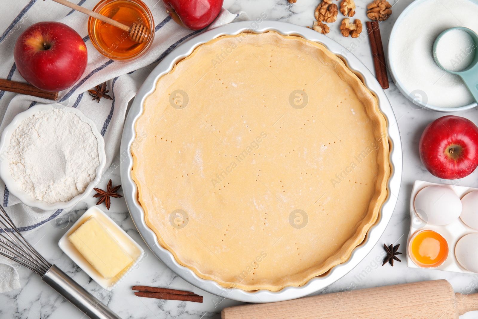 Photo of Raw dough and ingredients for traditional English apple pie on white marble table, flat lay