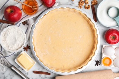 Raw dough and ingredients for traditional English apple pie on white marble table, flat lay