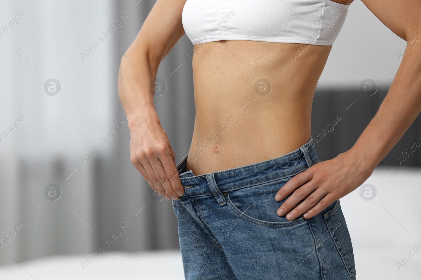 Photo of Slim woman wearing big jeans at home, closeup. Weight loss