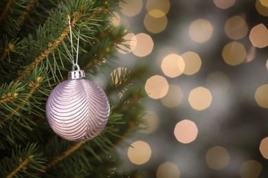 Photo of Shiny lilac ball hanging on Christmas tree against festive lights. Space for text