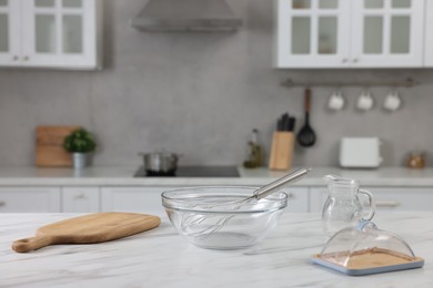 Photo of Whisk, bowl, board and other kitchen utensils on white marble table indoors, space for text