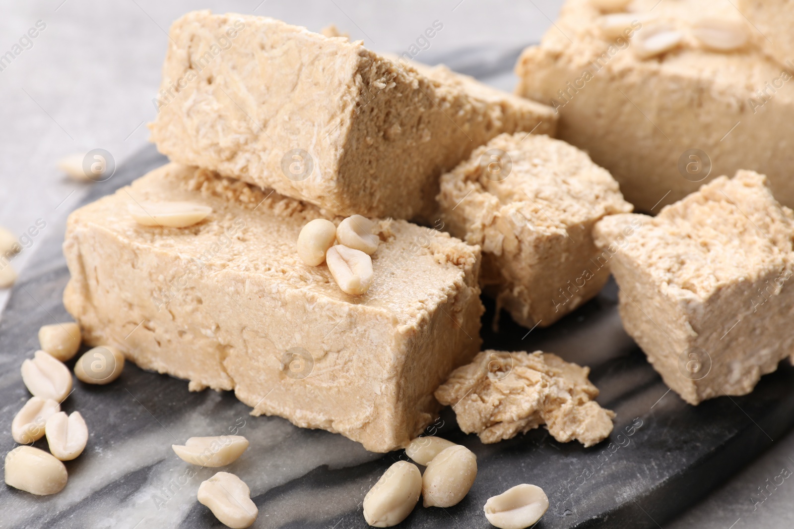 Photo of Pieces of tasty halva on dark gray marble board, closeup