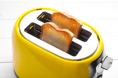 Photo of Yellow toaster with roasted bread on white wooden table, closeup