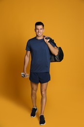 Handsome man with sports bag and bottle of water on yellow background