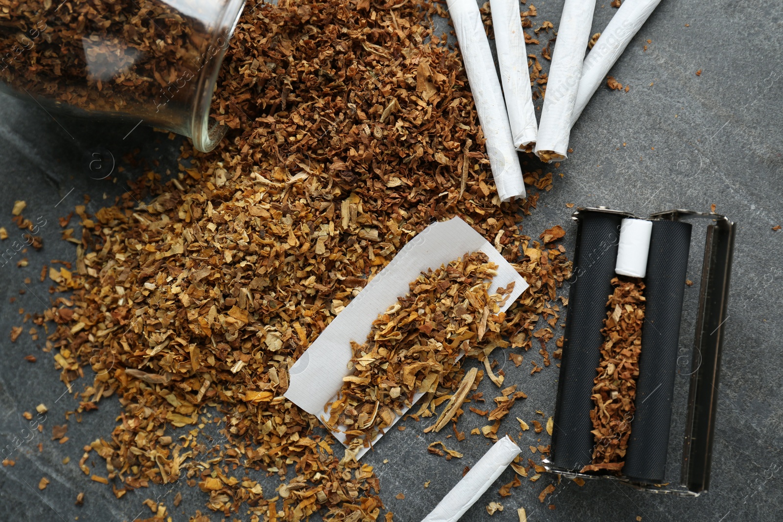 Photo of Flat lay composition with roller and tobacco on dark grey table. Making hand rolled cigarettes