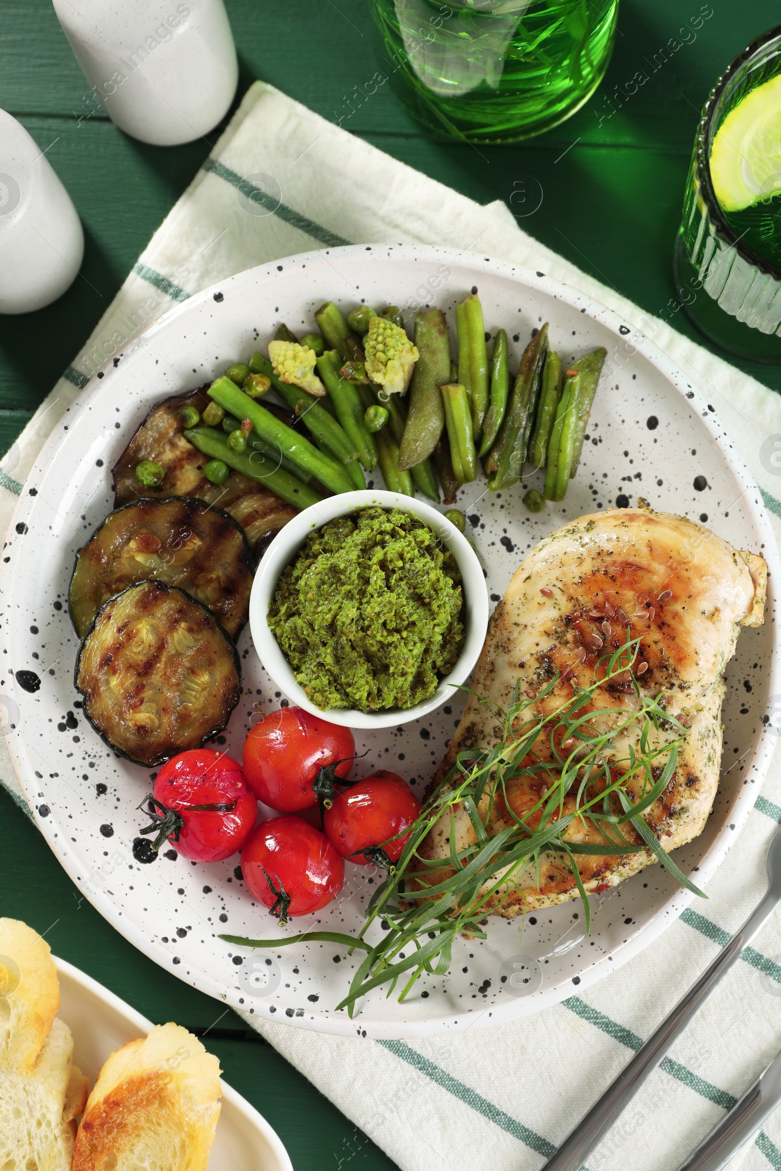 Photo of Tasty chicken, vegetables with tarragon and pesto sauce on green table, flat lay