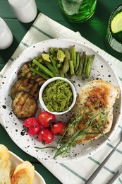 Photo of Tasty chicken, vegetables with tarragon and pesto sauce on green table, flat lay