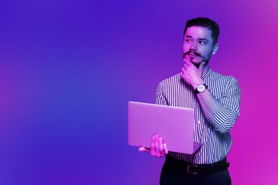 Handsome man with laptop in neon lights, space for text