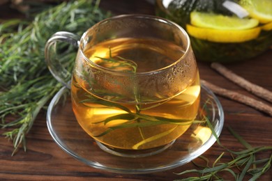 Cup of homemade herbal tea and fresh tarragon leaves on wooden table, closeup