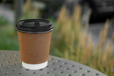 Photo of Paper cup of hot coffee on table outdoors, closeup with space for text. Takeaway drink