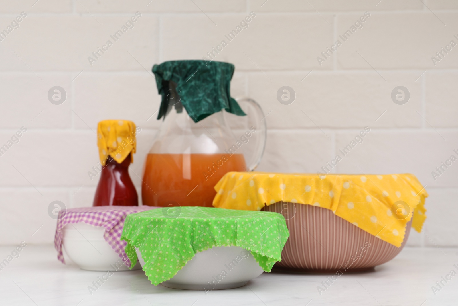 Photo of Different dishware covered with beeswax food wraps on white marble table